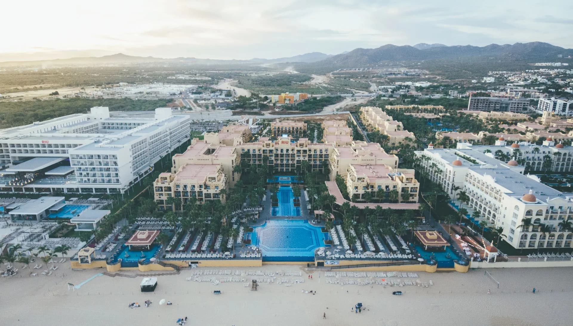 Hotels and beach umbrellas along Medano Beach in Cabo San Lucas, with El Arco in the distance