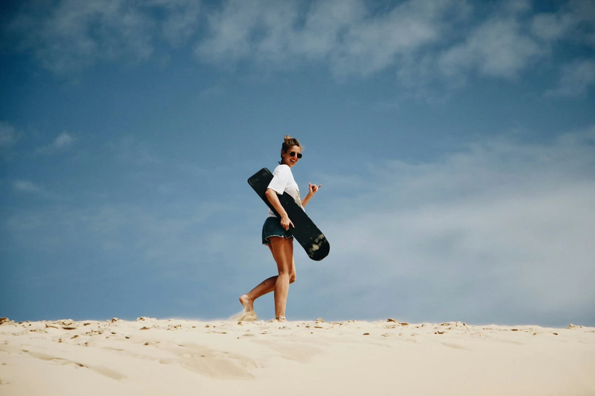 Person sandboarding down a steep dune at Las Dunas del Mogote in La Paz, Mexico at sunset