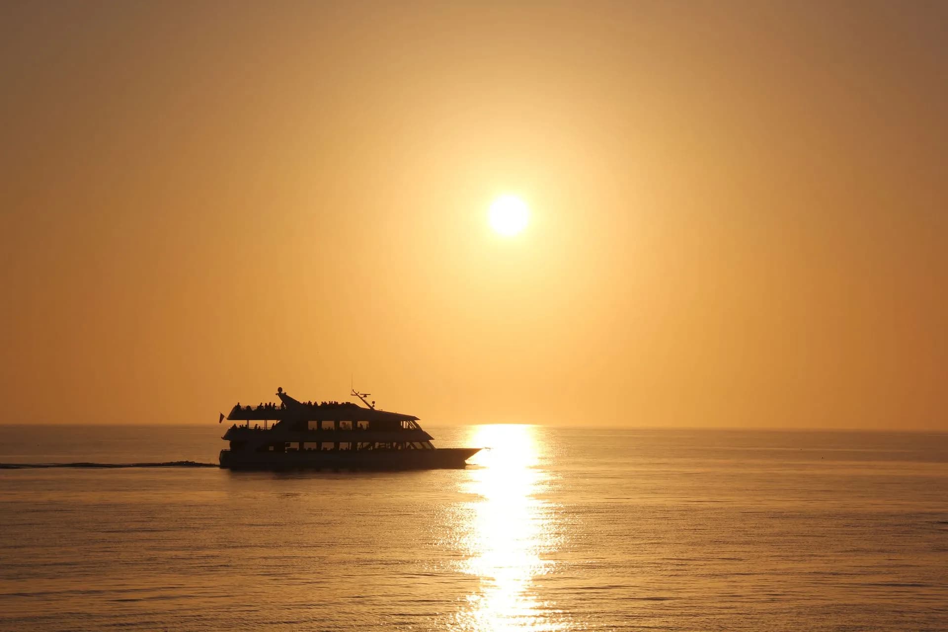 Catamaran sailing past El Arco at sunset in Cabo San Lucas with a golden sky over the water